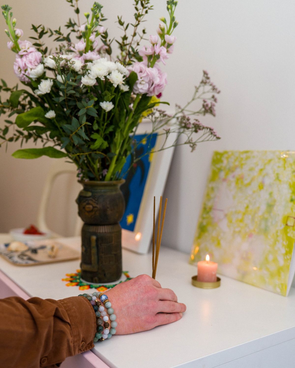Una mano enciende incienso junto a una vela y un ramo de flores, antes de una sesión de Mon Calme