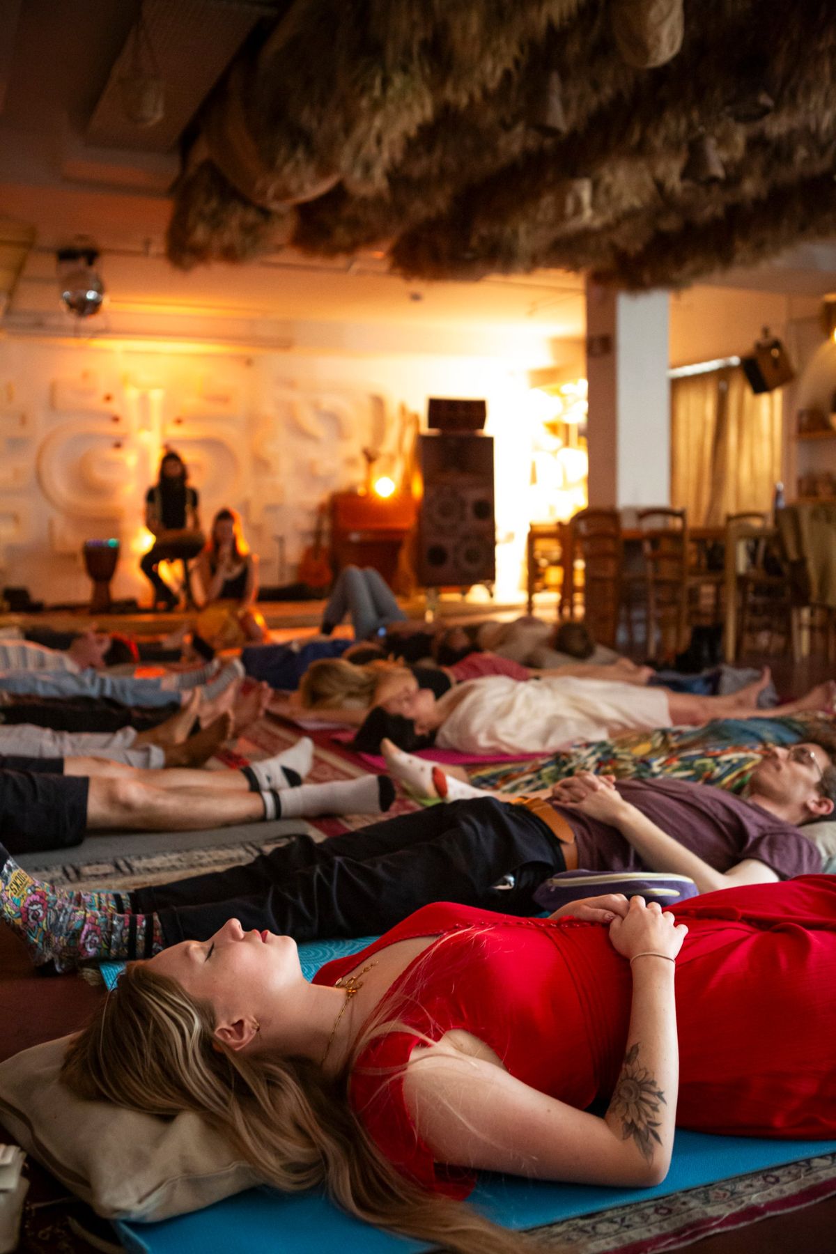 Participants allongés sur des tapis, yeux fermés, pendant un voyage sonore collectif dans une salle à la lumière chaude
